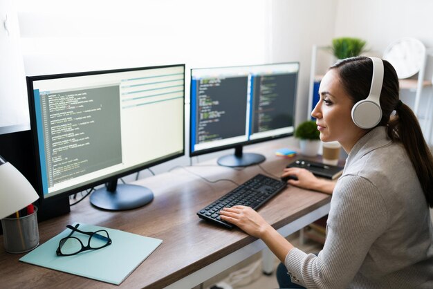 hispanic young woman with headphones coding a software app on the computer at home. freelance programmer writing code