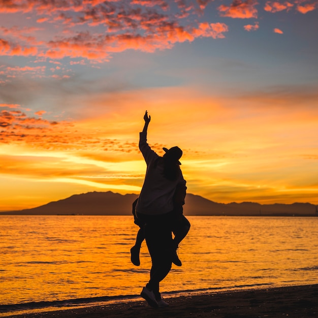 man holding woman on back on dark sea shore