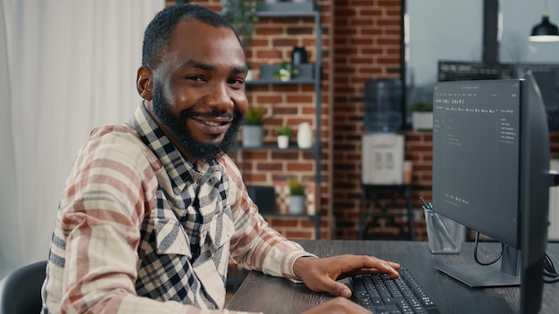 Software developer typing programming code on computer keyboard turning head and smiling while innovating online cloud computing. Casual programer sitting at desk writing code feeling confident.