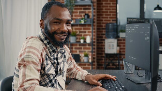 Software developer typing programming code on computer keyboard turning head and smiling while innovating online cloud computing. Casual programer sitting at desk writing code feeling confident.