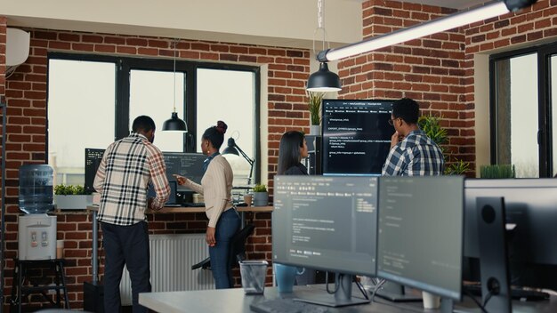 System developers analyzing code on wall screen tv looking for errors while team of coders collaborate on artificial intelligence project. Programmers working together at machine learning software.
