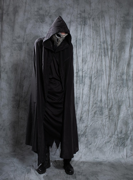 a gothic guy in a raven outfit a black cape with a hood and a bird mask