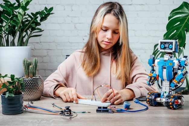 a teenager girl plugging cables to sensor chips while learning arduino coding and robotics