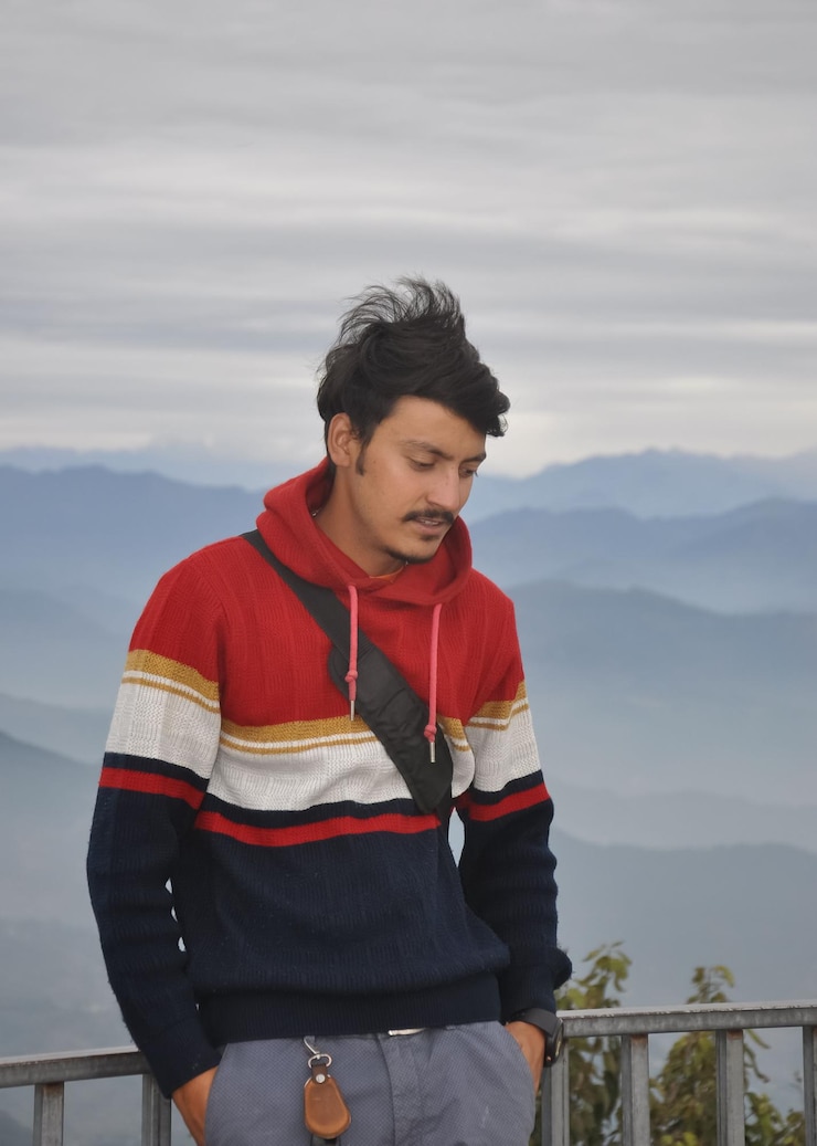 Photo a young guy looking down with hands in pocket while standing against the background of mountains