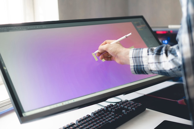 a young male digital artist drawing paint on the computer screen monitor in studio