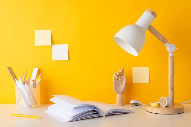 Academic preparations setup Side view photo of pencils pens rulers adhesive tape open reminder mannequin hand stapler lamp and sticky notes neatly arranged on a desk against yellow wall