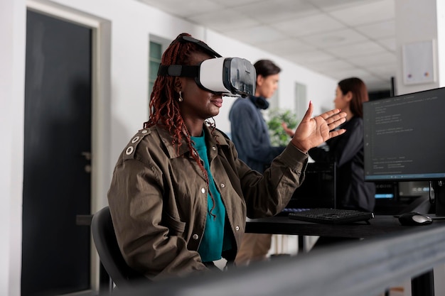 African american database admin working with virtual reality goggles to develop server app in it agency office, using source code. Checking programming language on cloud computing database, web develo