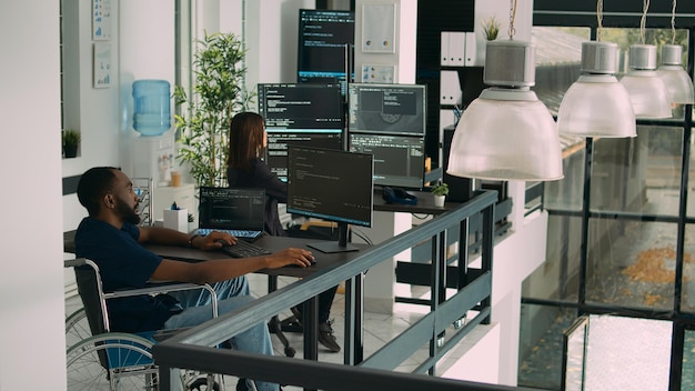 African american developer with impairment using computer to write code, parsing algorithm in software agency. Coder working on user interface with database in disability friendly office.