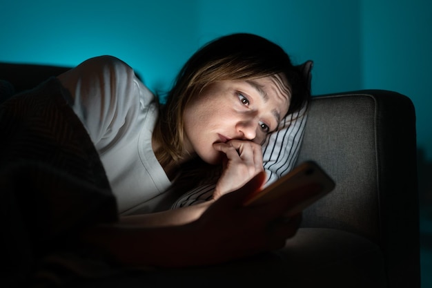 anxious woman in bed using smartphone at night can not stop scrolling news media before bedtime