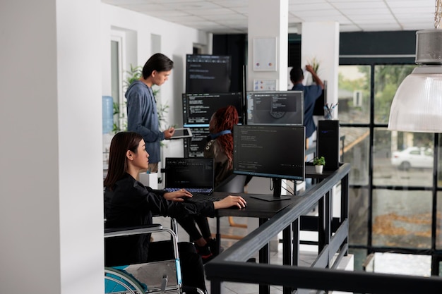 Asian disabled software programmer writing html code in agency big data room, using security system. Engineer with physical disability programming user interface artificial intelligence office.