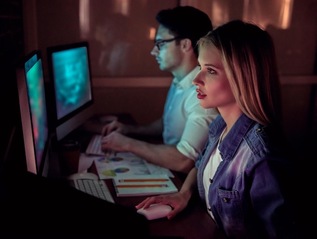 Beautiful young businessman and woman are working with computer in office at night