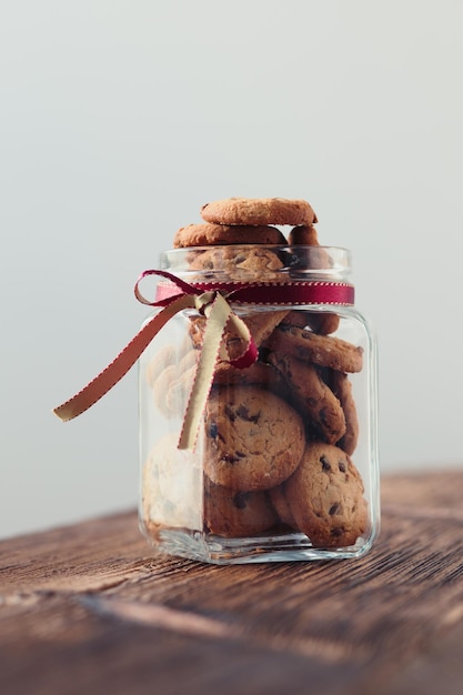 big jar filled with oat cookies standing on a wooden table plain background portrait orientation