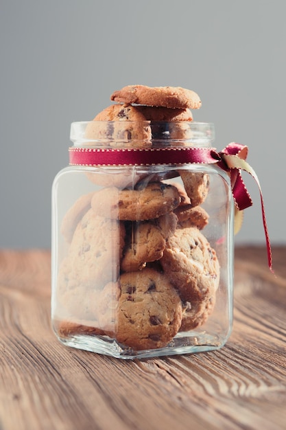 big jar filled with oat cookies standing on a wooden table plain background portrait orientation