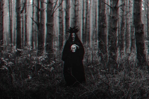 black terrible witch holds the skull of a dead man in her hands. black and white with 3d glitch virtual reality effect