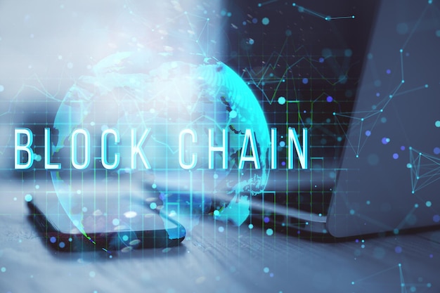 blockchain technology hologram over smartphone and laptop on table with glowing world map concept in background