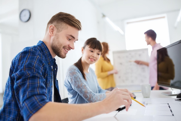business, startup and people concept - happy creative team with blueprint at office