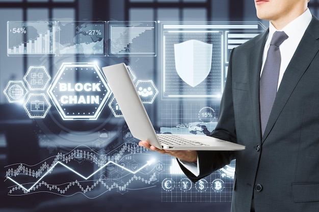Businessman using laptop with digital business interface in blurry office interior Technology and future concept Double exposure
