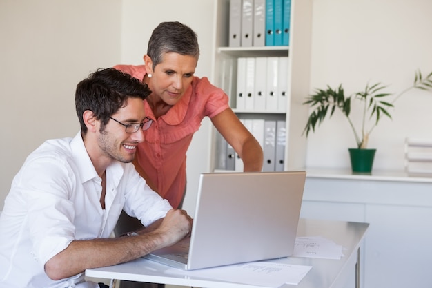 Casual business team working together at desk using laptop
