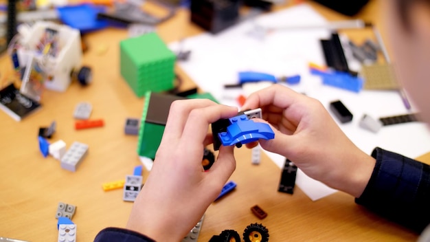 Close-up childrens hands hold a multicolored small robot machine assembled from a designer
