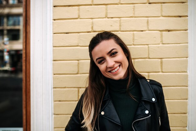 close-up image of smiling girl standing in front of a yellow wall.