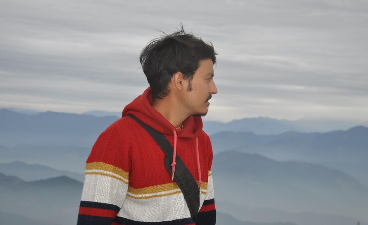 Photo close up of a handsome young guy looking sideways while posing against the background of mountains