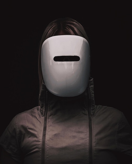 Close-up of woman wearing mask and hooded jacket against black background