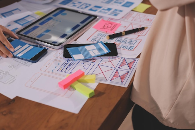 Close up ux developer and ui designer brainstorming about mobile app interface wireframe design on table with customer breif and color code at modern officeCreative digital development agency