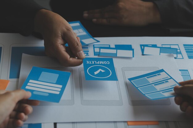 Close up ux developer and ui designer brainstorming about mobile app interface wireframe design on table with customer breif and color code at modern officeCreative digital development agency