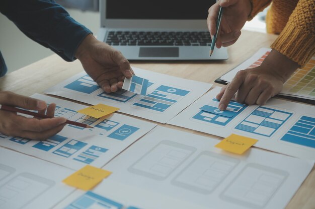 Close up ux developer and ui designer brainstorming about mobile app interface wireframe design on table with customer breif and color code at modern officeCreative digital development agency