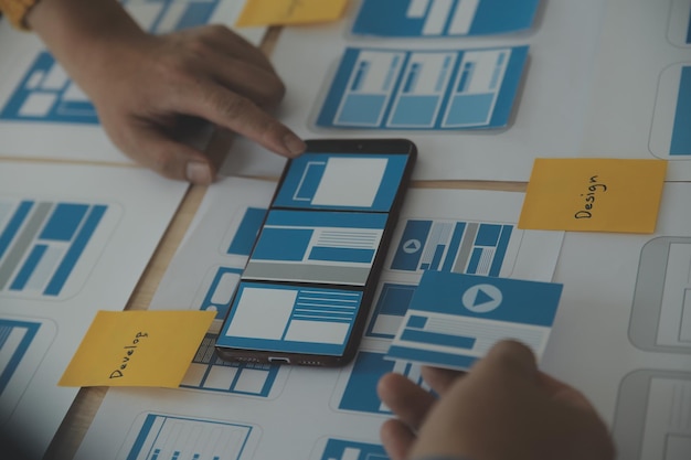 Close up ux developer and ui designer brainstorming about mobile app interface wireframe design on table with customer breif and color code at modern officeCreative digital development agency