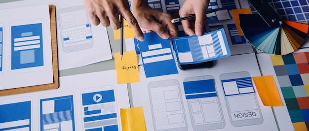 Close up ux developer and ui designer brainstorming about mobile app interface wireframe design on table with customer breif and color code at modern officeCreative digital development agency
