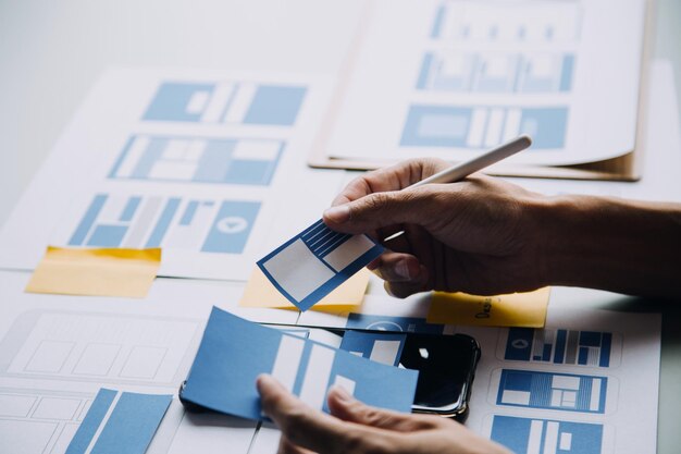 Close up ux developer and ui designer brainstorming about mobile app interface wireframe design on table with customer breif and color code at modern officeCreative digital development agency