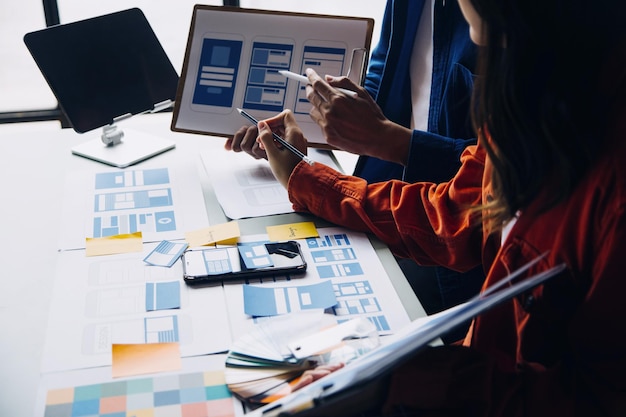 Close up ux developer and ui designer brainstorming about mobile app interface wireframe design on table with customer breif and color code at modern officeCreative digital development agency