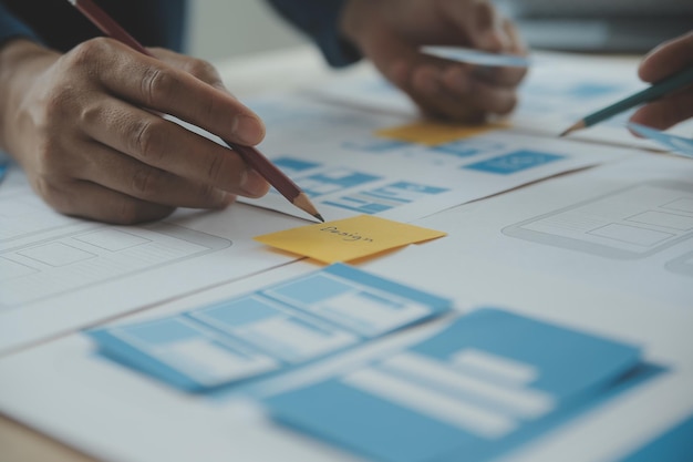 Close up ux developer and ui designer brainstorming about mobile app interface wireframe design on table with customer breif and color code at modern officeCreative digital development agency