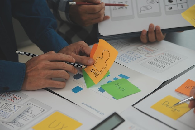 Close up ux developer and ui designer brainstorming about mobile app interface wireframe design on table with customer breif and color code at modern officeCreative digital development agency