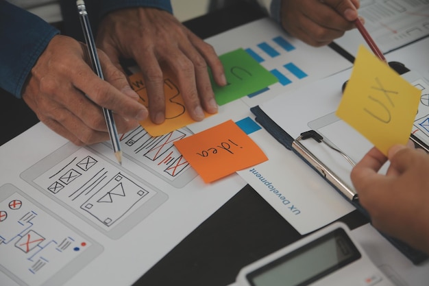 Close up ux developer and ui designer brainstorming about mobile app interface wireframe design on table with customer breif and color code at modern officeCreative digital development agency