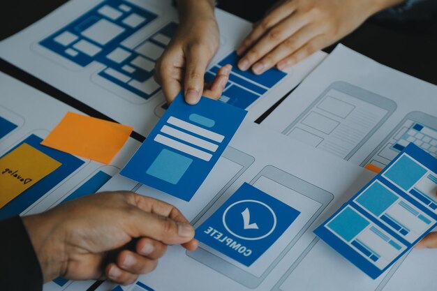 Close up ux developer and ui designer brainstorming about mobile app interface wireframe design on table with customer breif and color code at modern officeCreative digital development agency
