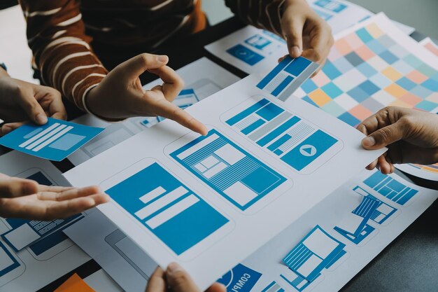Close up ux developer and ui designer brainstorming about mobile app interface wireframe design on table with customer breif and color code at modern officeCreative digital development agency