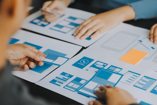 Close up ux developer and ui designer brainstorming about mobile app interface wireframe design on table with customer breif and color code at modern officeCreative digital development agency