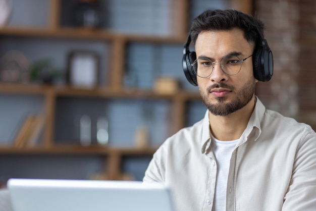 Closeup photo of a serious and focused young indian man wearing headphones working and studying on a