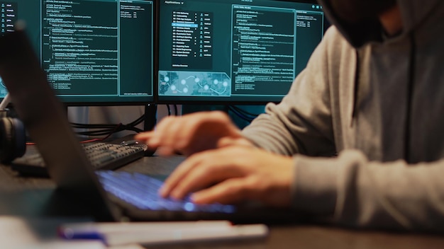 Coder nguy hiểm xâm nhập hệ thống bảo mật để đánh cắp dữ liệu lớn, lập trình để xâm phạm mạng trực tuyến. Mã hóa virus để tạo phần mềm độc hại và đột nhập vào máy chủ, sử dụng nhiều màn hình. Ảnh cầm tay.