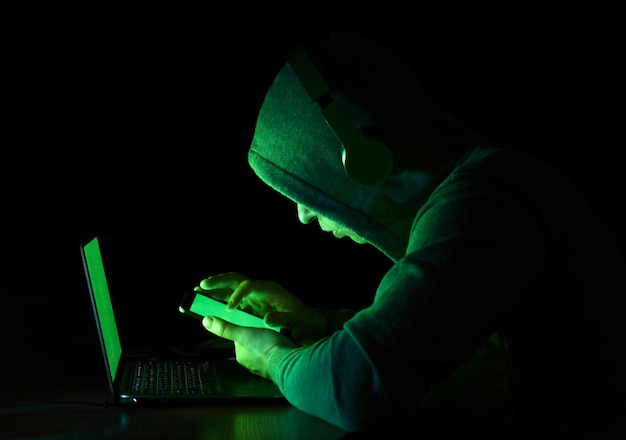 computer hacker using mobile phone and laptop against black background