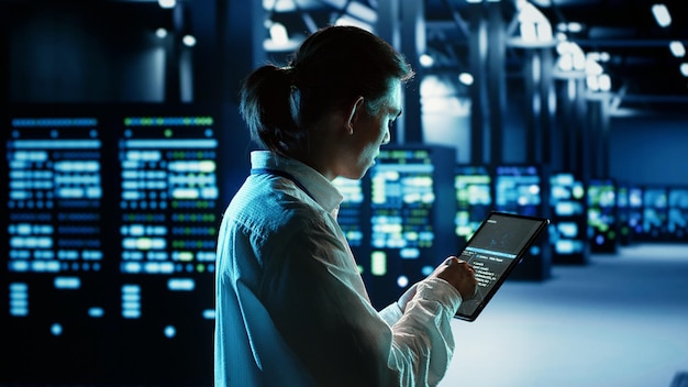 Computer scientist running code and programming on laptop, troubleshooting and upgrading server room equipment designed to accommodate mainframes, networking systems and storage arrays