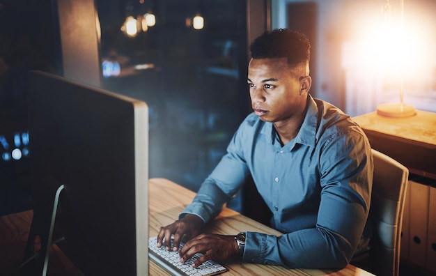 dark office and black man at computer typing online research or web programmer at tech startup night planning and network developer writing email coding or business report at digital agency