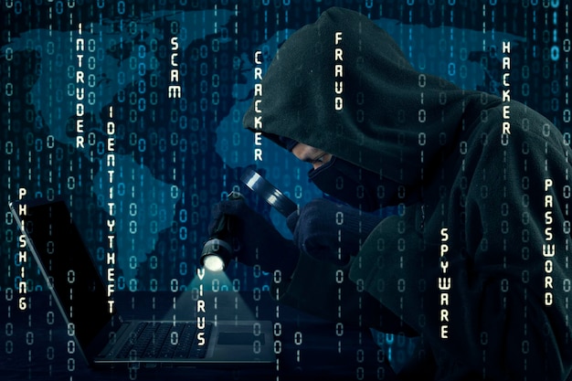 Digital composite image of computer hacker holding illuminated flash light and magnifying glass over laptop