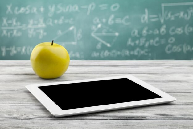 digital tablet and apple on the desk in front of blackboard