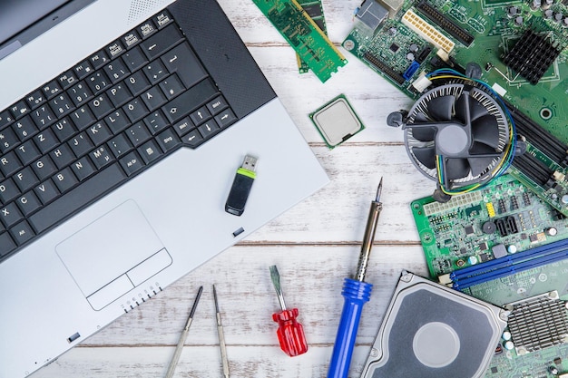 Directly above shot of laptop with mother board and work tools on white table