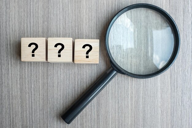 Directly above shot of magnifying glass with question marks on table