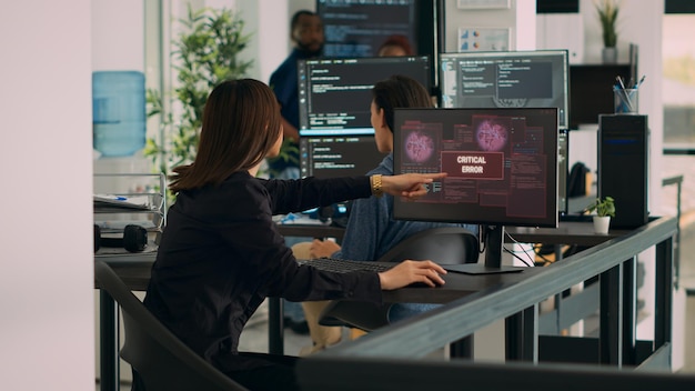 Diverse team of coders having server hacked and system crash, running critical error message flashing on screen with multiple monitos. Displaying hacking alert warning, cyber crime.