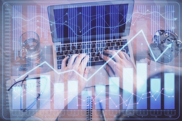 double exposure of mans hands typing over laptop keyboard and forex chart hologram drawing top view financial markets concept